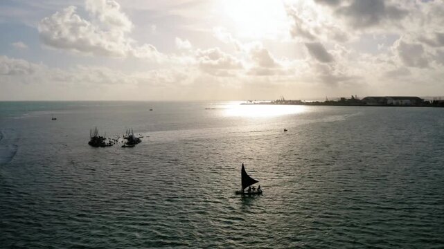 Silhouette of a small sailboat sailing on the ocean at sunset