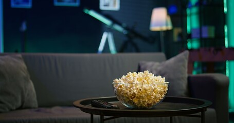 Snack prepared for movie night in dimly illuminated modern apartment home theatre. Empty neon lit cozy residential interior with sofa and bowl of popcorn on coffee table. © DC Studio