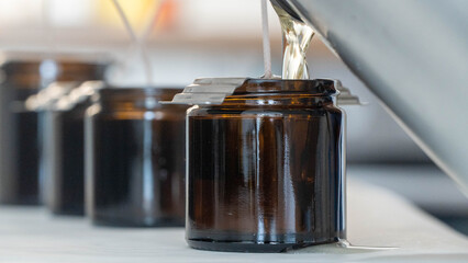 Candle making process pouring melted wax into brown glass jars with wicks
