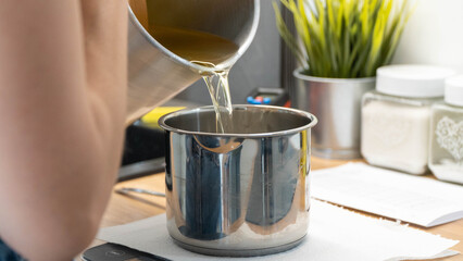 Pouring melted wax into stainless steel pot for candle making at home
