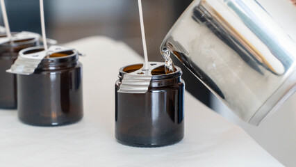 Candle making process pouring melted wax into brown glass jars with wicks