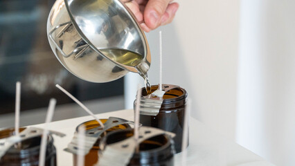 Candle making process pouring melted wax into brown glass jars with wicks
