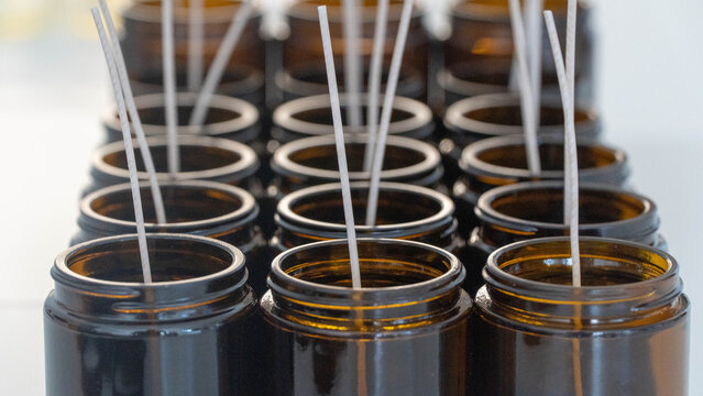 Rows of handcrafted candles with wicks in amber glass jars, ready for pouring.