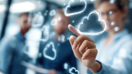 User interacting with a touchscreen display showing cloud storage icons in sharp focus with outoffocus colleagues collaborating in the background.