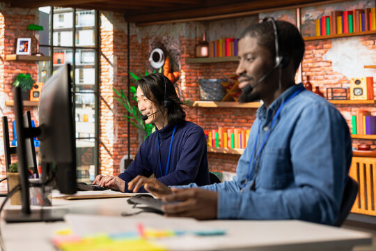 Multiethnic customer service colleagues tracking support ticket in dedicated company software on PC. Multiracial workers in diverse call center office creating support ticket for customer calling