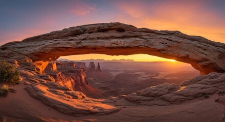 Rock arch formation at sunset overlooking a canyon landscape with warm light.