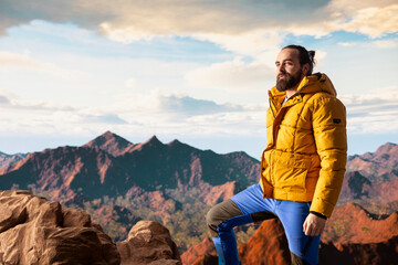 Naklejka premium Determined traveler enjoys the solitude of a mountain summit, where the panoramic view represents adventure and personal growth. Hiker with outdoor gear feeling cold on the windy mountain top.