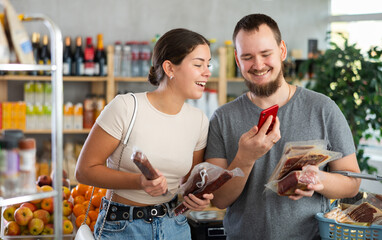 Married couple scan a package of deli meats. Husband and wife choose Spanish ham for dinner.