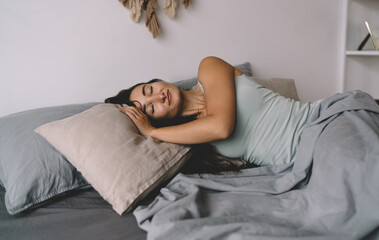 Brunette woman enjoying restful sleep at home, arms folded under pillow, gentle smile on face, representing emotional security, slow living and balance in everyday routine.