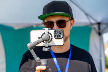 Young man records video using smartphone mounted on handheld gimbal stabilizer outdoors