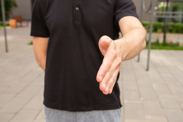 Fototapeta premium young caucasian man in a black polo shirt reaching out with his hand for a handshake outside