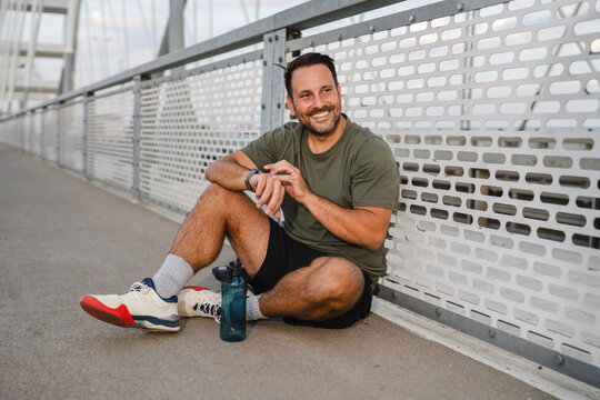 Male athlete resting on bridge checking smart watch