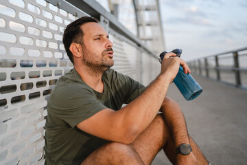 Male athlete resting after training, staying hydrated on bridge