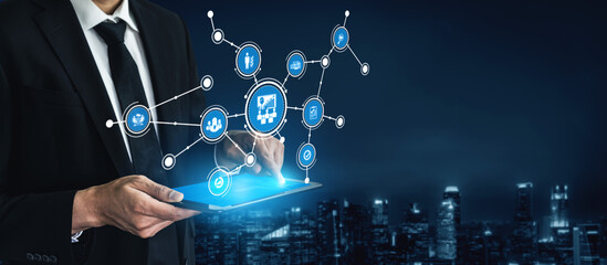 A businessman in a suit interacts with a digital tablet, showcasing technology and business analysis through abstract icons against a night cityscape. Tessel