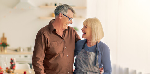 Affectionate senior couple looking at each other while cooking turkey for Christmas or Thanksgiving dinner at home. Happy elderly spouses preparing traditional holiday meal in kitchen