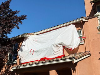 Protective plastic sheeting taped with red adhesive covering upper windows and stucco wall of suburban house during renovation