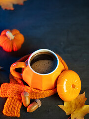 Orange cup of hot coffee with knitted scarf on table with pumpkin and maple leaves