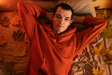 Portrait of a young man in an autumn home atmosphere. Maple yellow leaves are cut on the bed.