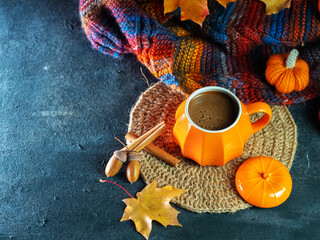 Autumn coziness, a cup of hot coffee on the table with a knitted warm scarf, pumpkin and maple leaves
