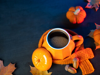 Orange cup of hot coffee with knitted scarf on table with pumpkin and maple leaves