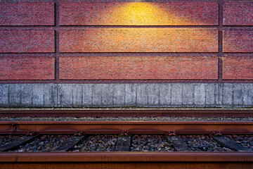 Railway beside brick wall with warm lamp flaring across tracks