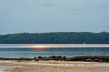 Sunny beach with stones and service pipe leading to calm sea at Solitude Flensburg