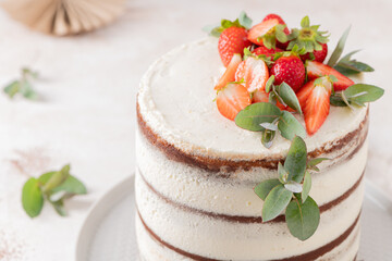 Handmade semi-naked cake adorned with creamy frosting, fresh strawberries, and natural eucalyptus leaves, ideal for celebrations