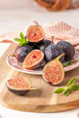 Sliced and whole figs on a plate and a wooden board with stevia leaves and a pink napkin in a rustic setting