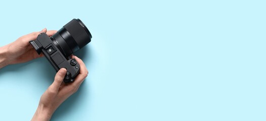 Hands holding modern professional photo camera on blue background with space for text © Pixel-Shot