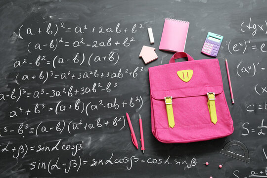 Pink school backpack with calculator, notebook and pens on black chalkboard painted with formulas - Powered by Adobe