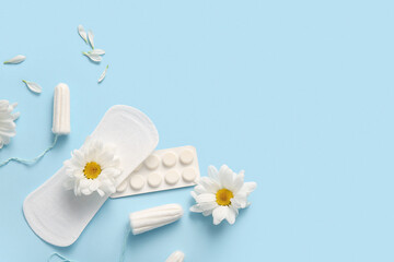 Menstrual pad with tampons, pills and chamomile flowers on blue background