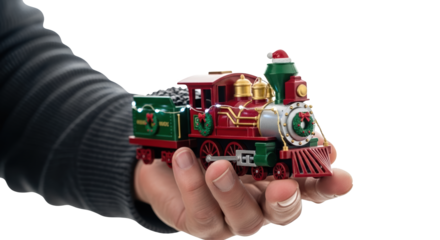 A hand holds a small, festive toy train decorated with christmas ornaments, isolated on transparent background
