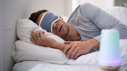 Man sleeping with smart ring, sleep tracking wearable, digital health device, eye mask and sleep monitor, wellness technology, modern rest accessory, nighttime recovery, smart sleep environment