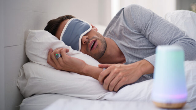 Man sleeping with smart ring, sleep tracking wearable, digital health device, eye mask and sleep monitor, wellness technology, modern rest accessory, nighttime recovery, smart sleep environment