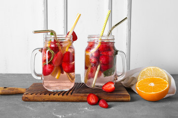 Mason jars of fresh infused water with strawberries, orange and lemon on grey table