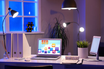 Laptop with abbreviation SEO on desk in dark office