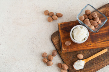 Wooden board with shea butter and nuts on light background
