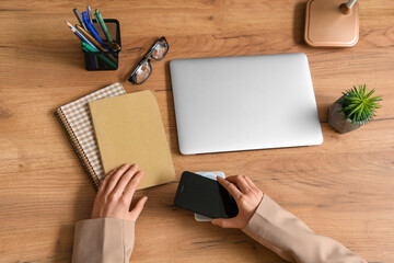 Female hands with modern gadgets and stationery on wooden background