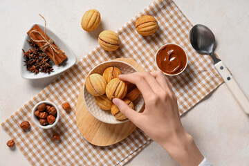 Woman taking tasty walnut shaped cookies with boiled condensed milk on white grunge table