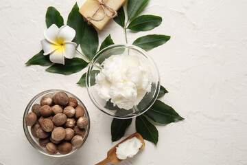 Glass bowl of shea butter with nuts and soap bar on white background