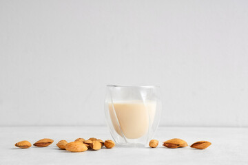 Glass of fresh almond milk and nuts on white background