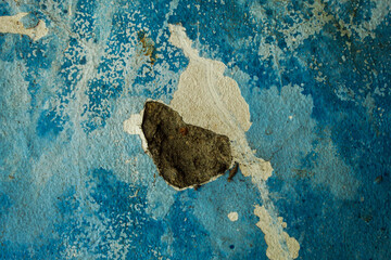 wall texture with peeling and cracked blue paint, revealing a layer of gray cement plaster