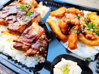 豚バラの角煮と鶏肉の唐揚げが乗った二段重ねの美味しそうな弁当です。ご飯の上にタレとゴマがかかっており、付け合わせのポテトサラダも添えられています。