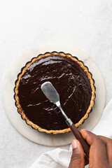 Overhead view of chocolate ganache filled tart shell, top view of chocolate filling in a baked pie shell, process of making chocolate tart