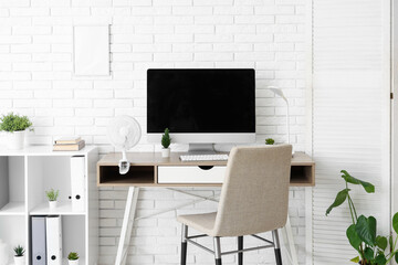 Modern electric fan on table near white brick wall in office