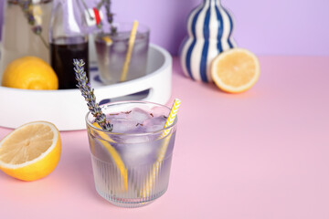 Glass of fresh lavender lemonade with flowers and lemons on colorful background