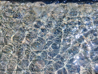 日差しが降り注ぐ水面のクローズアップ写真です。波紋が重なり、太陽の光が反射してキラキラと輝き、美しい抽象的な光景を作り出しています。