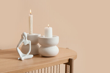 Burning candles with figurine on dresser near beige wall in living room