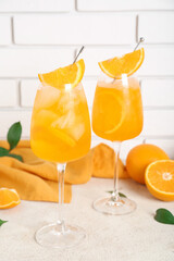 Glasses of Aperol spritz cocktail with oranges and leaves on white table