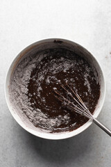 Overhead view of flour and cocoa powder being whisked into chocolate batter, process of making chocolate mud cake, making a dark chocolate cake